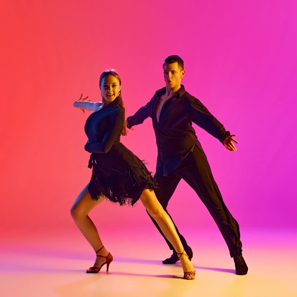 Two dancers in black mid-step against a backdrop fading from red to pink