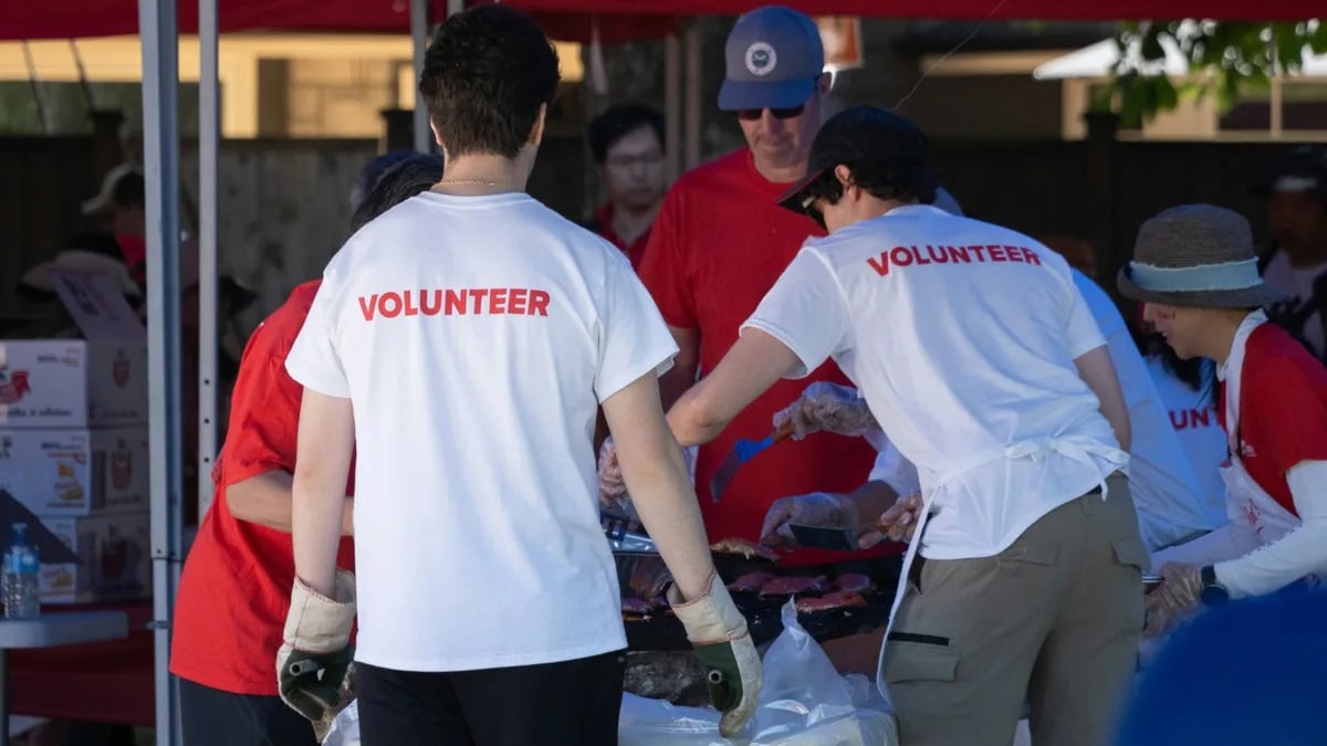 Volunteers in white Volunteer shirts working a barbecue under blue gazebos