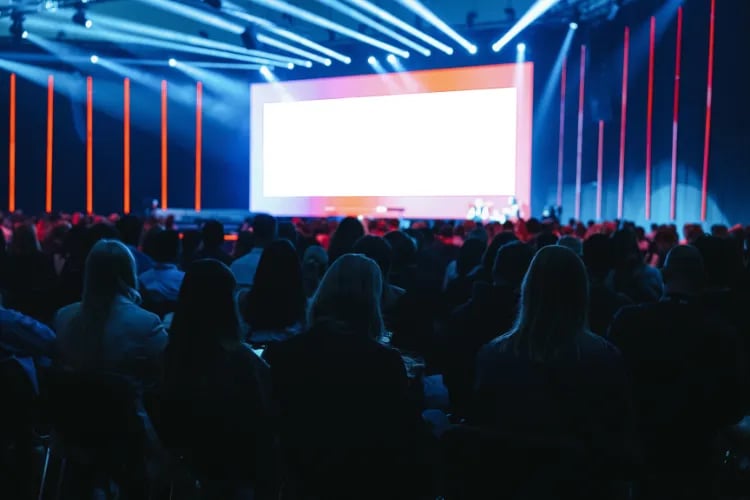 A modern event space filled with attendees at a product launch event, with stage lighting and branded visuals.