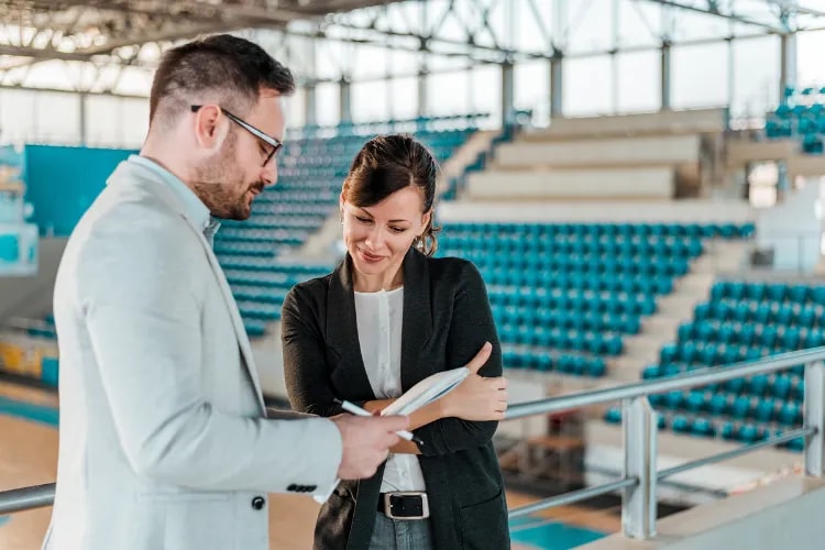 Event Organizer standing in a sports venue and holding contract, next to the venue manager