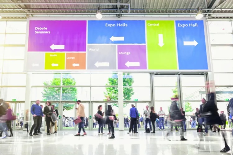 A wide shot of a tadeshow with signs showing where to go